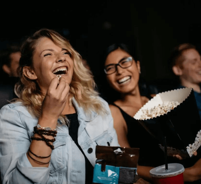 two woman watching movie with popcorn and laughing