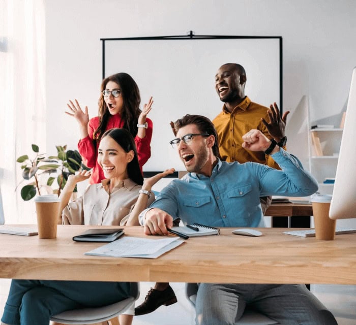 Coworkers sitting at a desk high fiving each other and cheering on