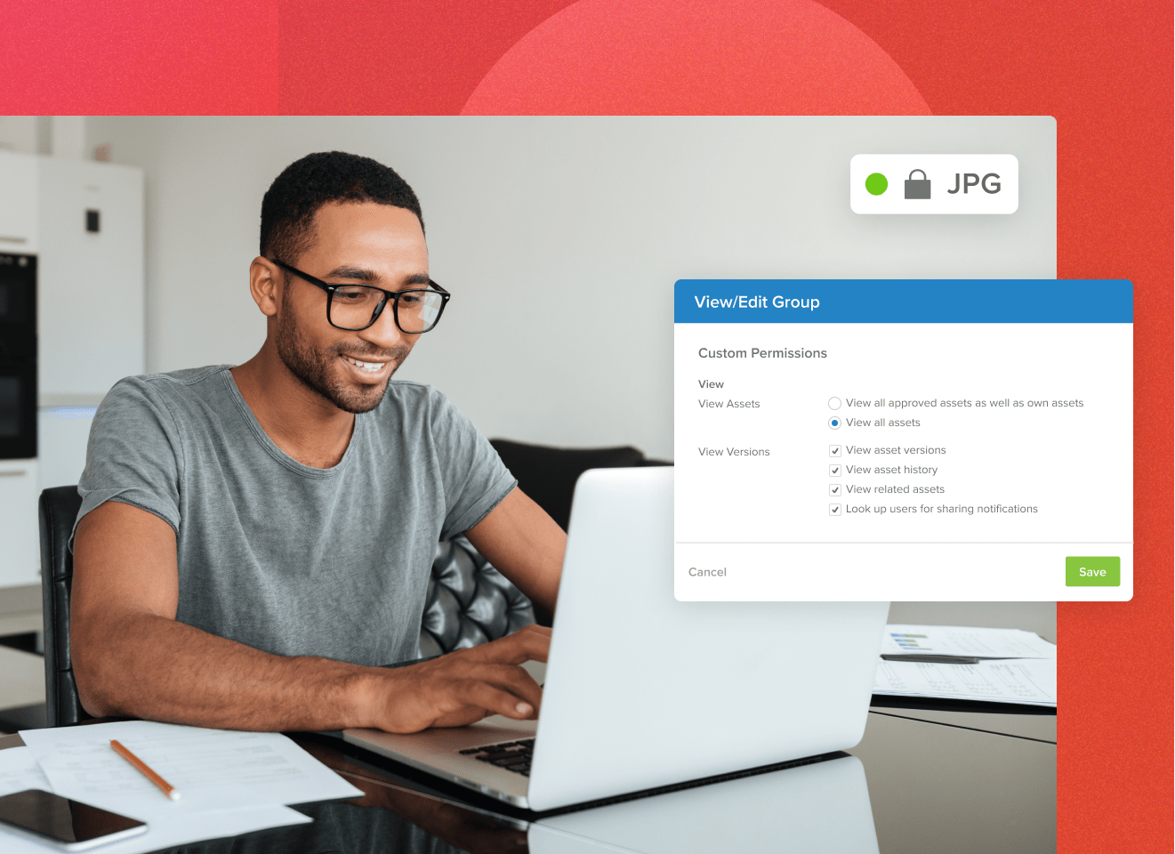 Man with glasses on a laptop working at a table smiling with a View/Edit Group popup showing MediaValet custom permissions on a jpg file with a red background