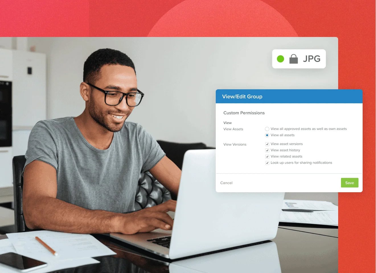 Man with glasses on a laptop working at a table smiling with a View/Edit Group popup showing MediaValet custom permissions on a jpg file with a red background