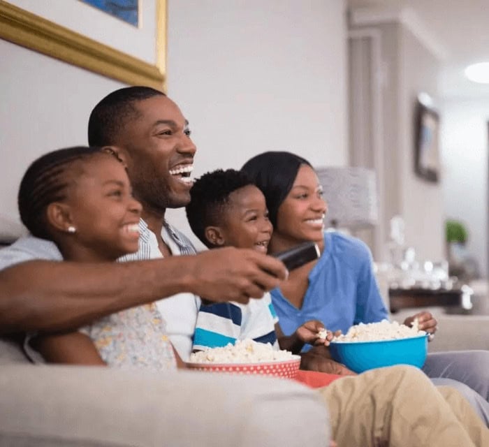 A family laughing and eating popcorn watching a movie on the couch