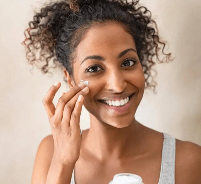 A woman putting cream on her face and smiling