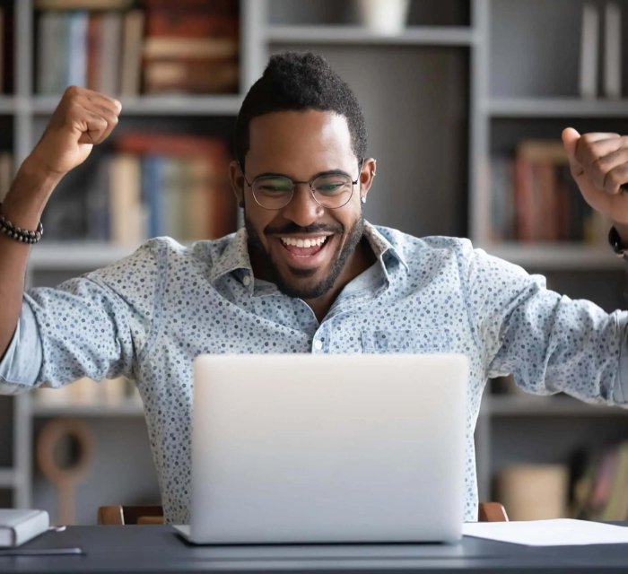 A man cheering while looking at his laptop and sitting at a desk