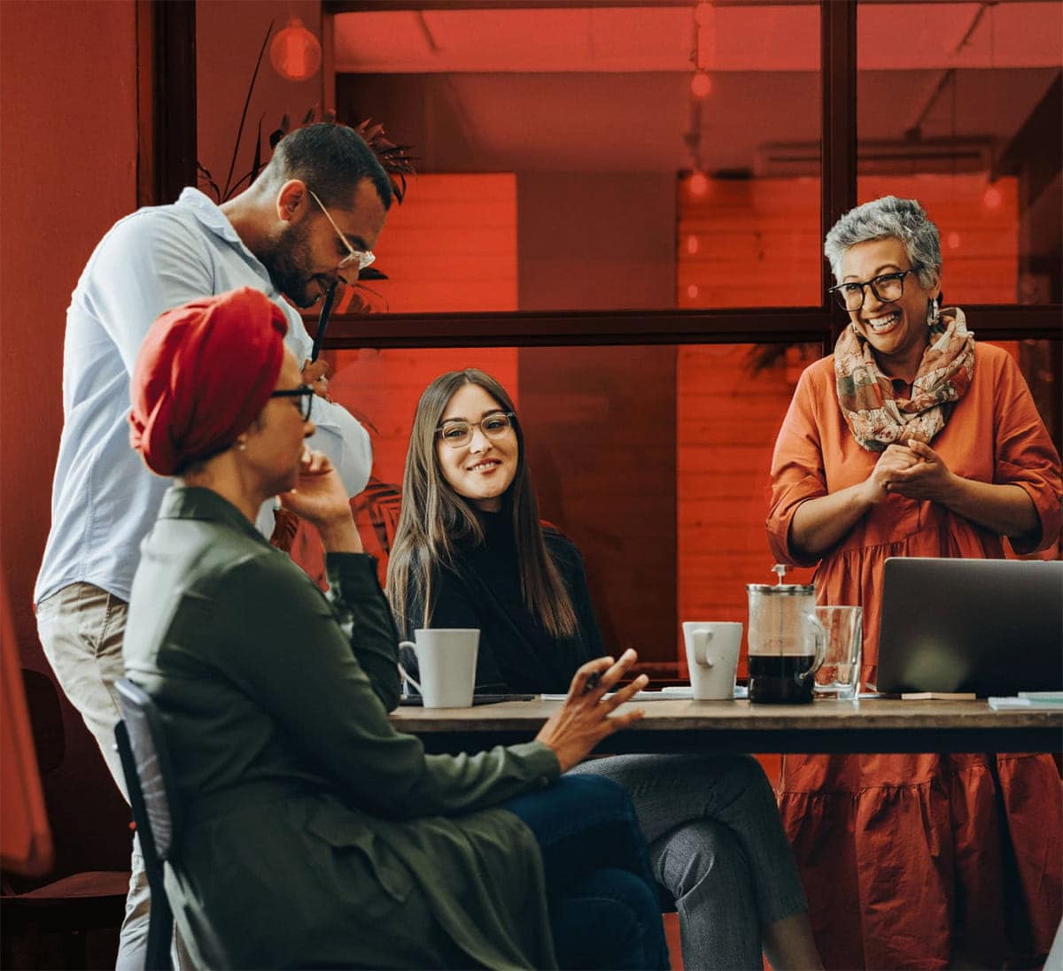 Group of people around a meeting room table, laughing and having coffee