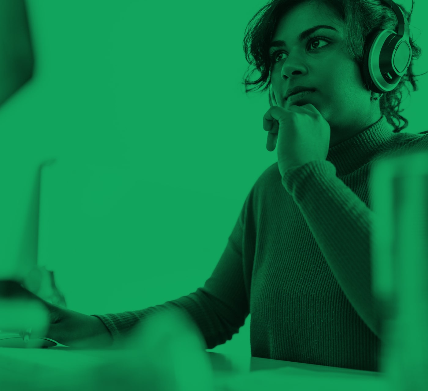Woman with her chin in her hand looking at a laptop on a desk. Set on a green background,