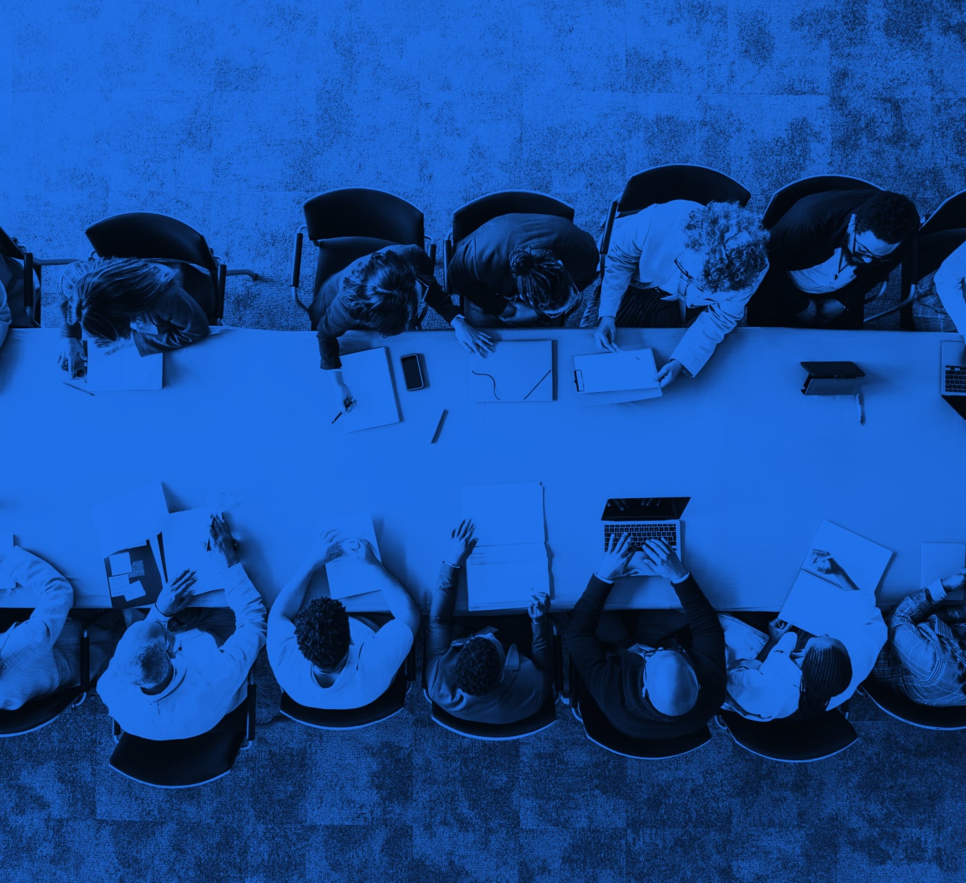A group of 10 people sitting around a board table discussing complex project workflows. With a blue overlay on the image