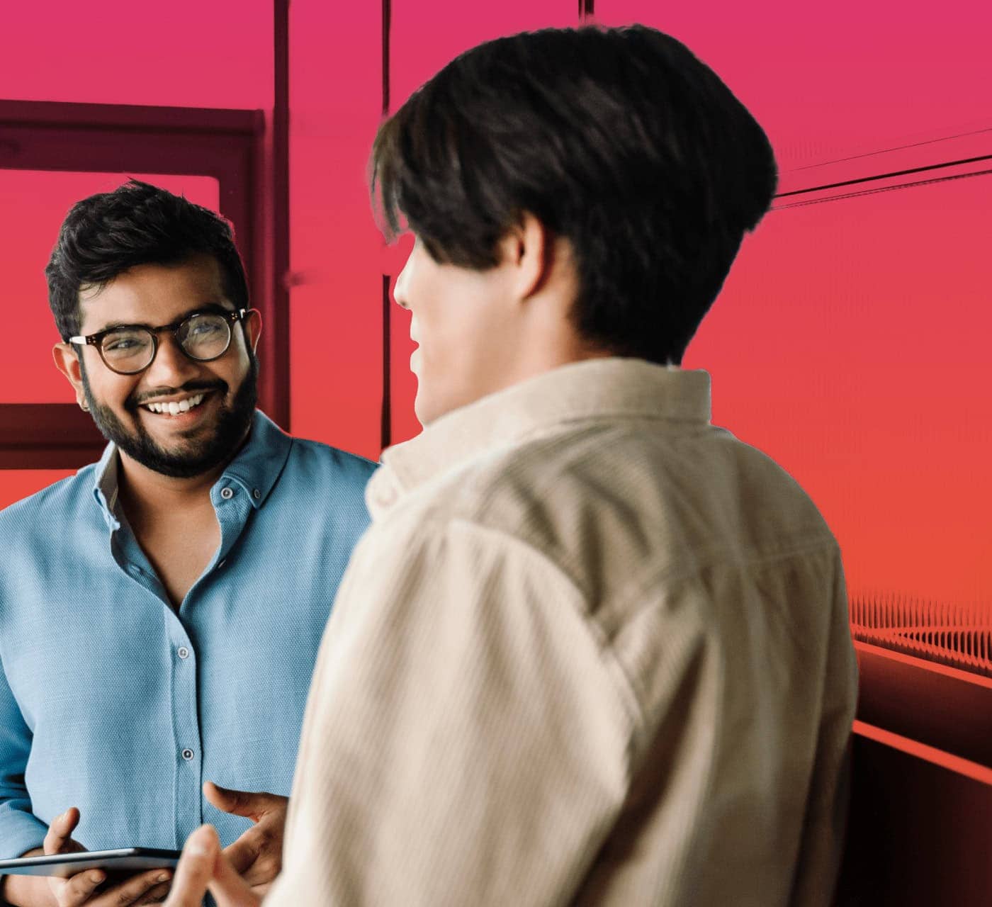 two male colleagues facing each other with an ipad in one of their hands having a conversation on a red magenta gradient background