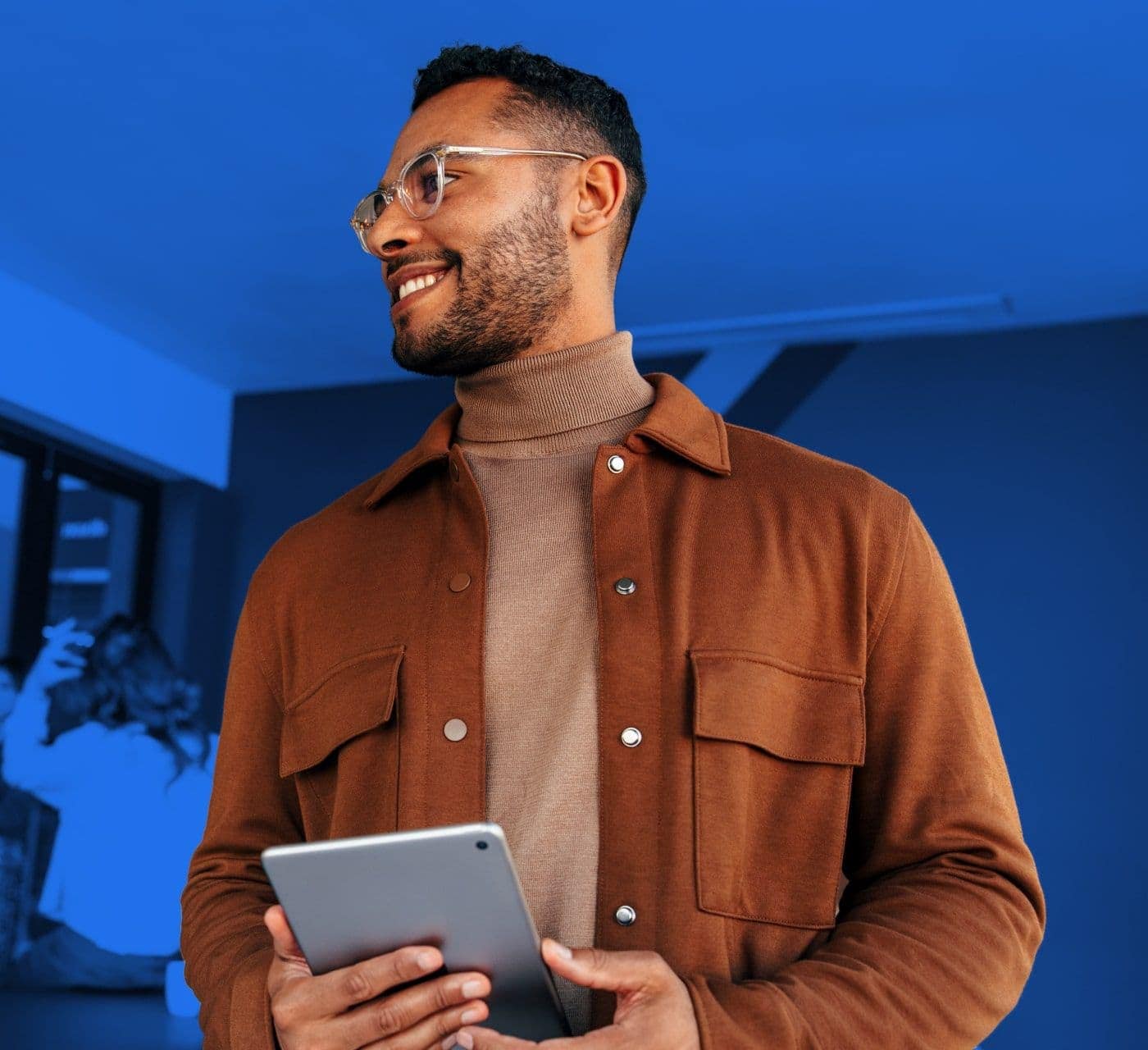 man in glasses holding an ipad looking to his right on a blue background
