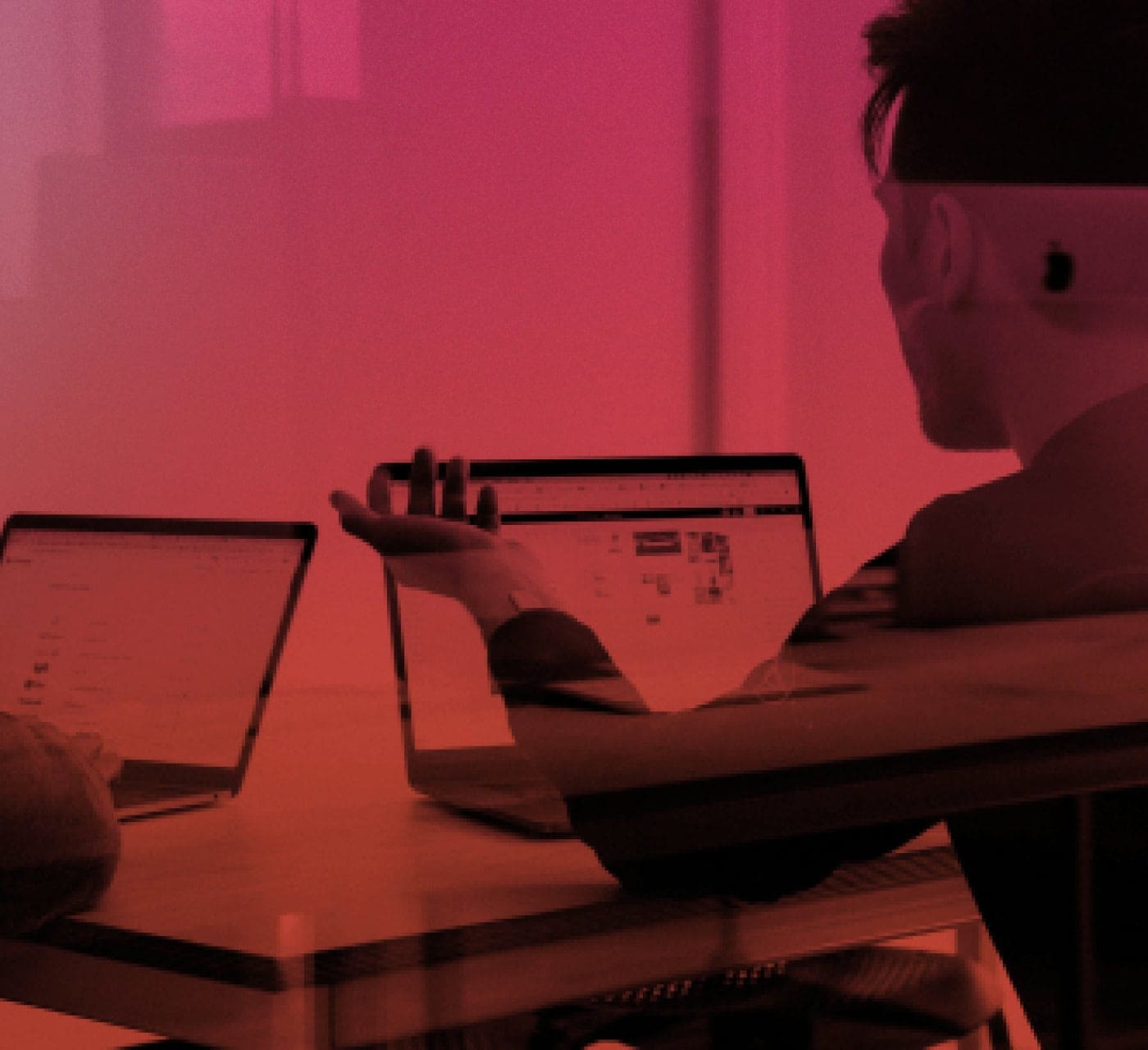 magenta red gradient image of two colleagues having a discussion over their laptops