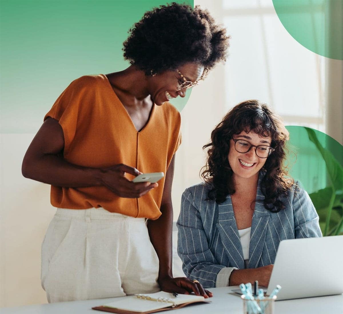 Two smiling women in an office looking at a laptop screen