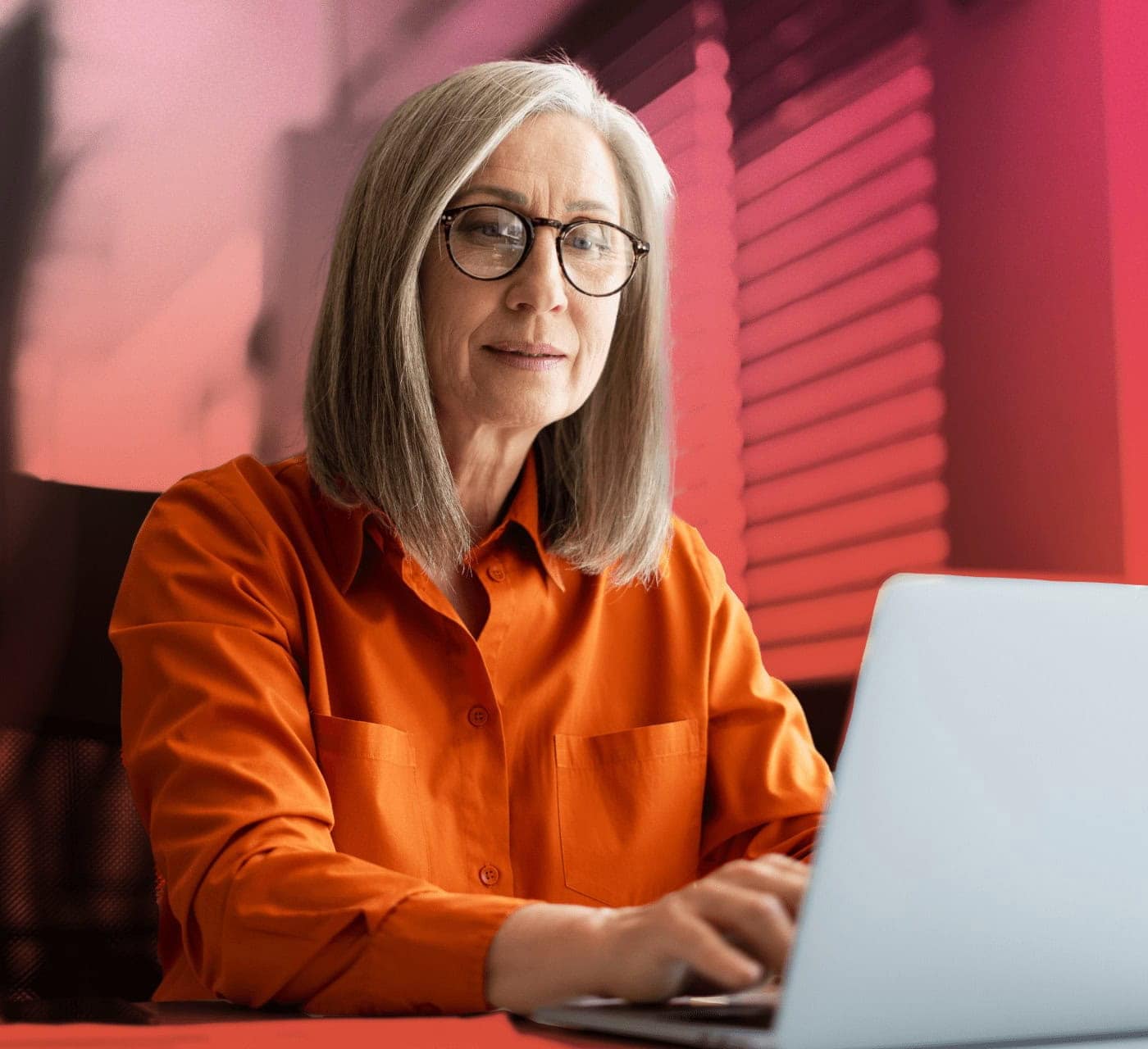 Business woman wearing an orange top working on a laptop