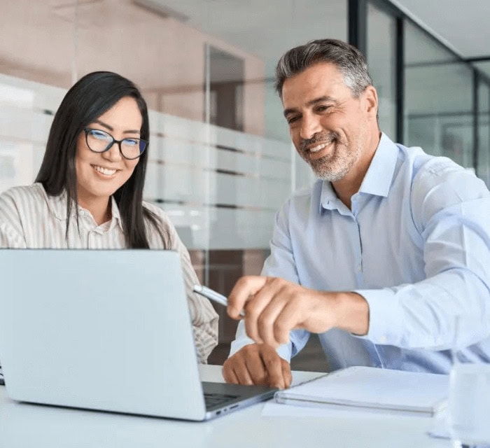 a man and a woman at work looking at a laptop and smiling while doing work